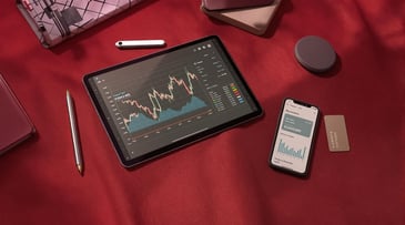 Tablet and smartphone displaying financial graphs and data analysis on a red background with stationery items.